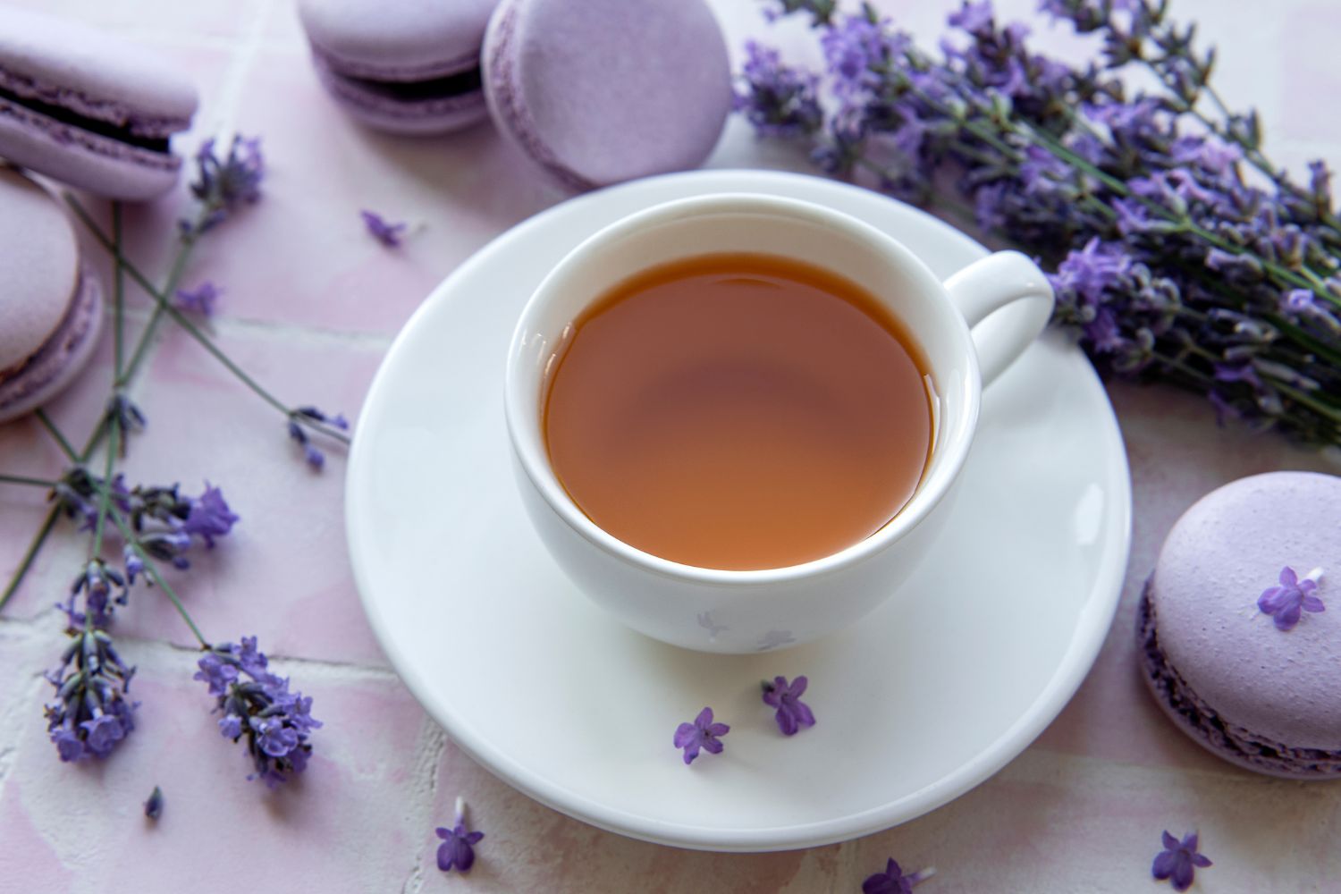 Tea in white teacup and saucer with purple macarons and lavender flowers beside it.